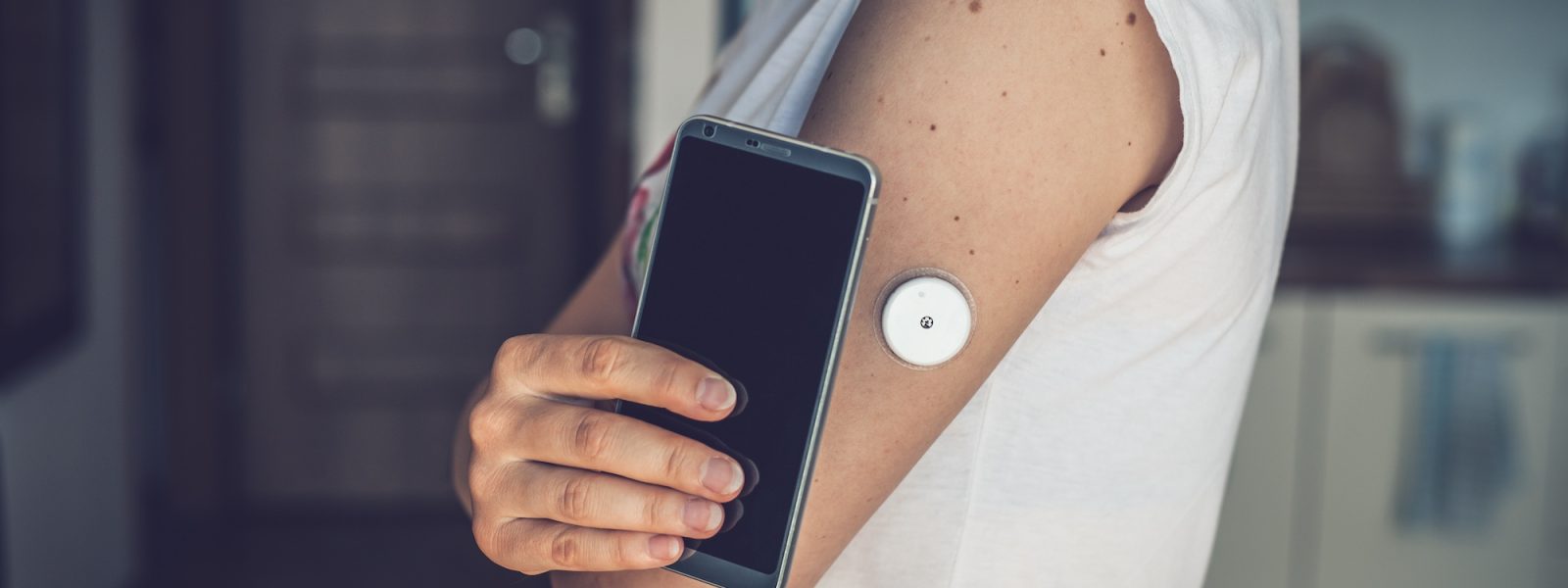 Woman checking glucose level with a remote sensor and mobile phone, sensor checkup glucose levels without blood. Diabetes treatment.