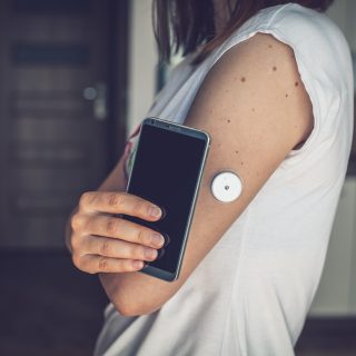 Woman checking glucose level with a remote sensor and mobile phone, sensor checkup glucose levels without blood. Diabetes treatment.
