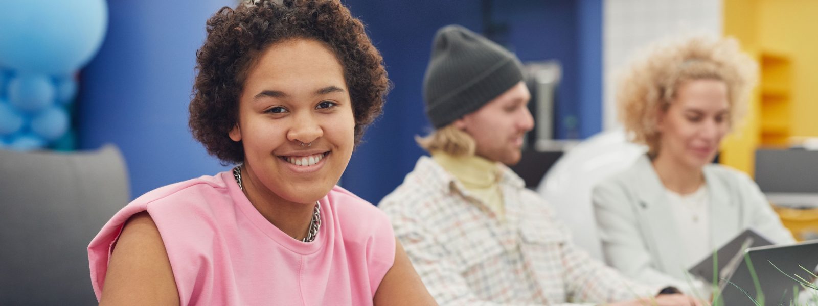 Young woman sitting at a table with other young adults in the background.
