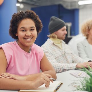 Young woman sitting at a table with other young adults in the background.